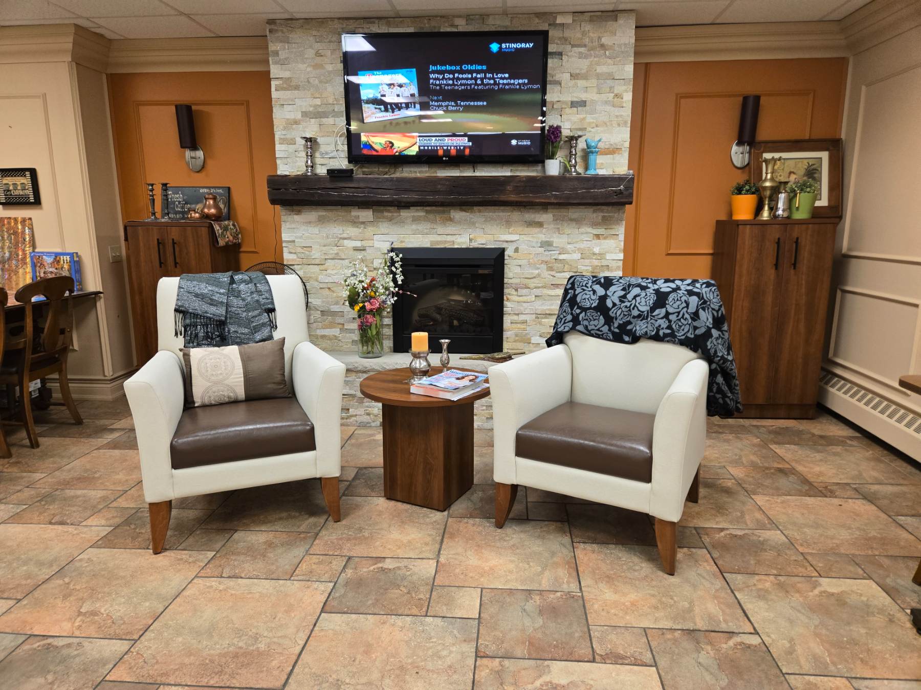 Common-area lounge with IntelliCare lounge seating and a round walnut occasional table by the fireplace